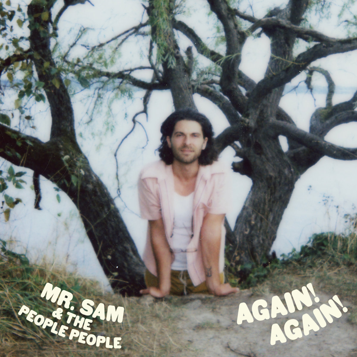 Man in pink shirt leaning hands on ground, looking forward with a big live oak tree in the background.