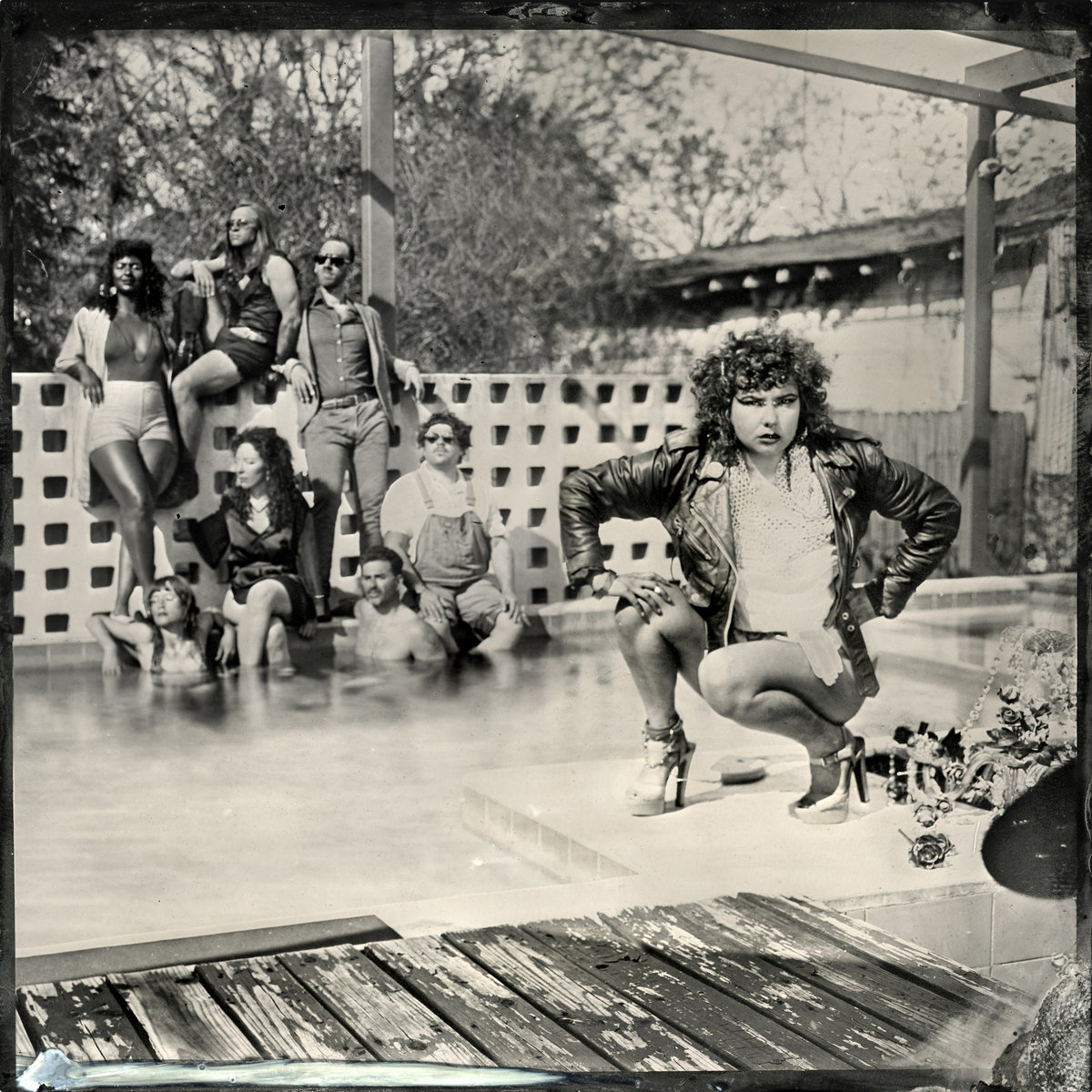 A black and white photo of a woman in a leather jacket squats in front of a group of people. 